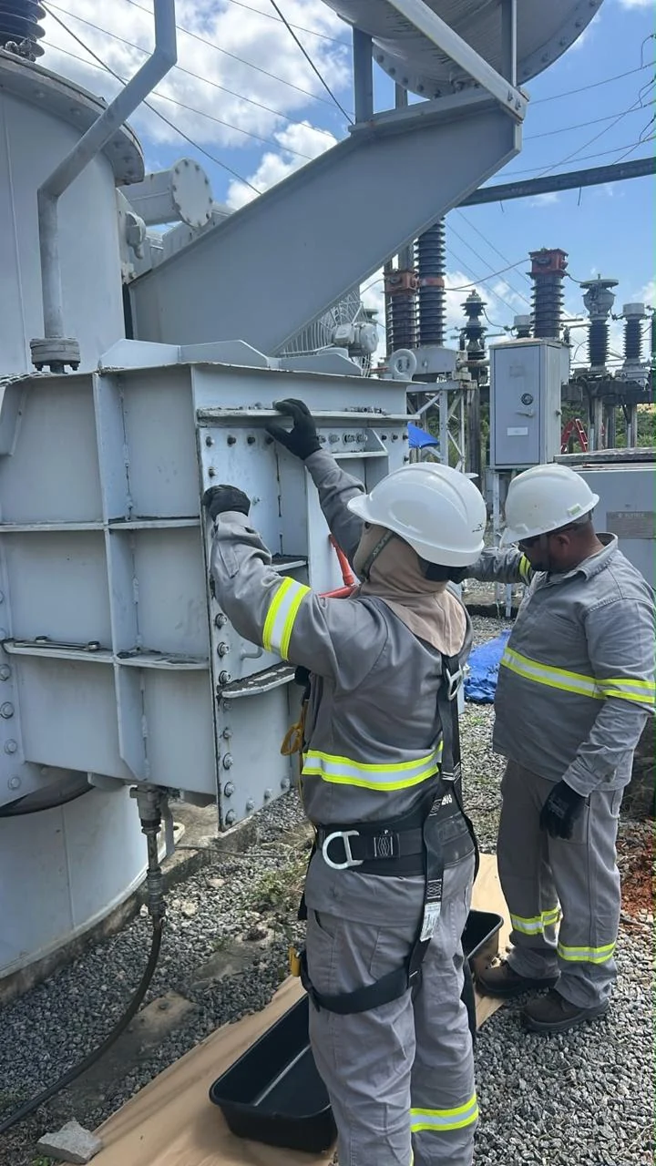 Equipe realizando trabalho junto à lateral de um transformador